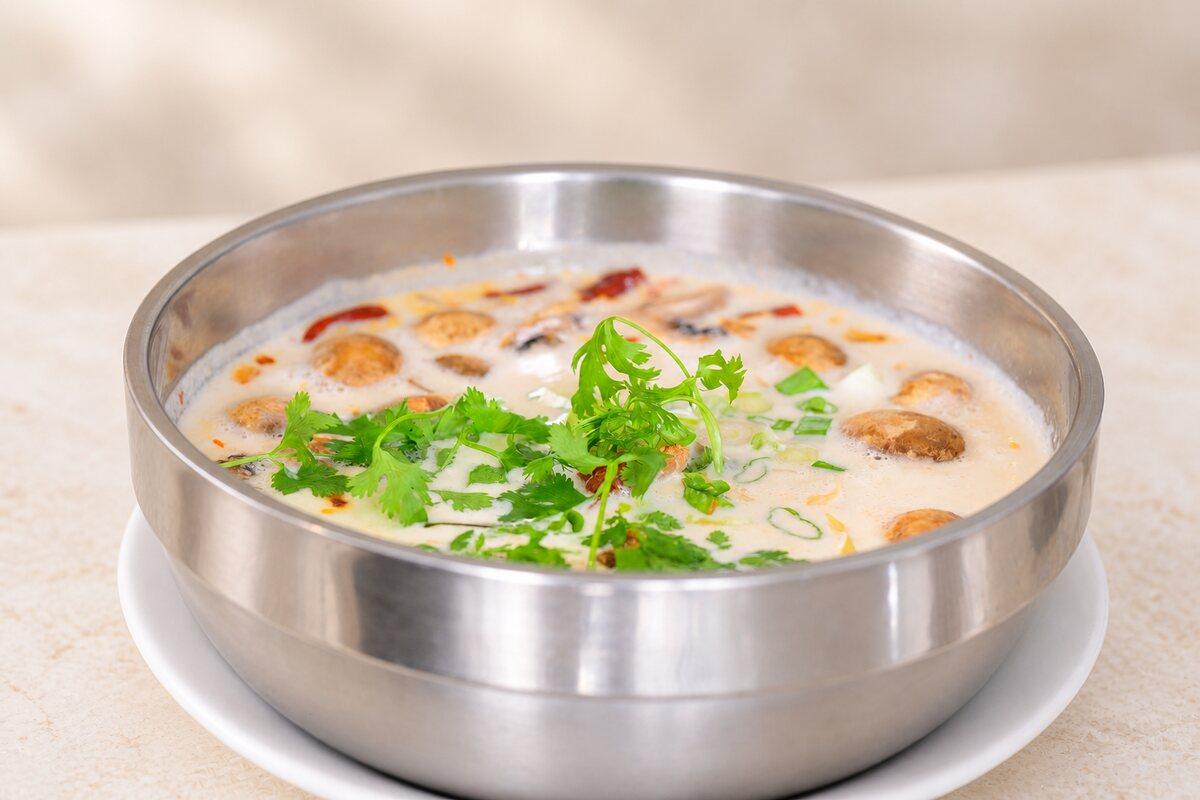 A steel bowl of creamy coconut soup with mushrooms and fresh coriander.