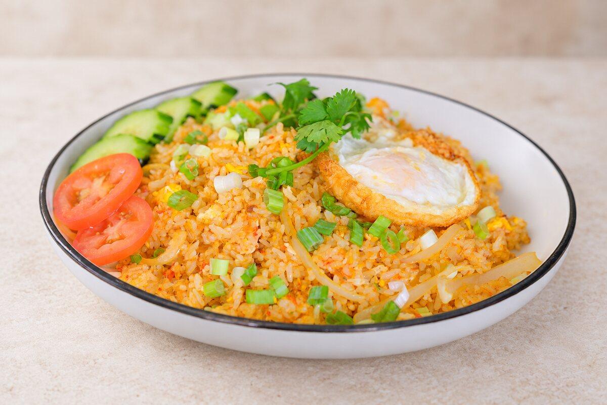 Fried rice topped with a fried egg, with cucumber and tomato on the side.