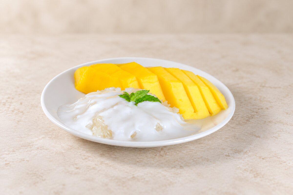 Sliced ripe mango beside coconut sticky rice with a mint leaf.