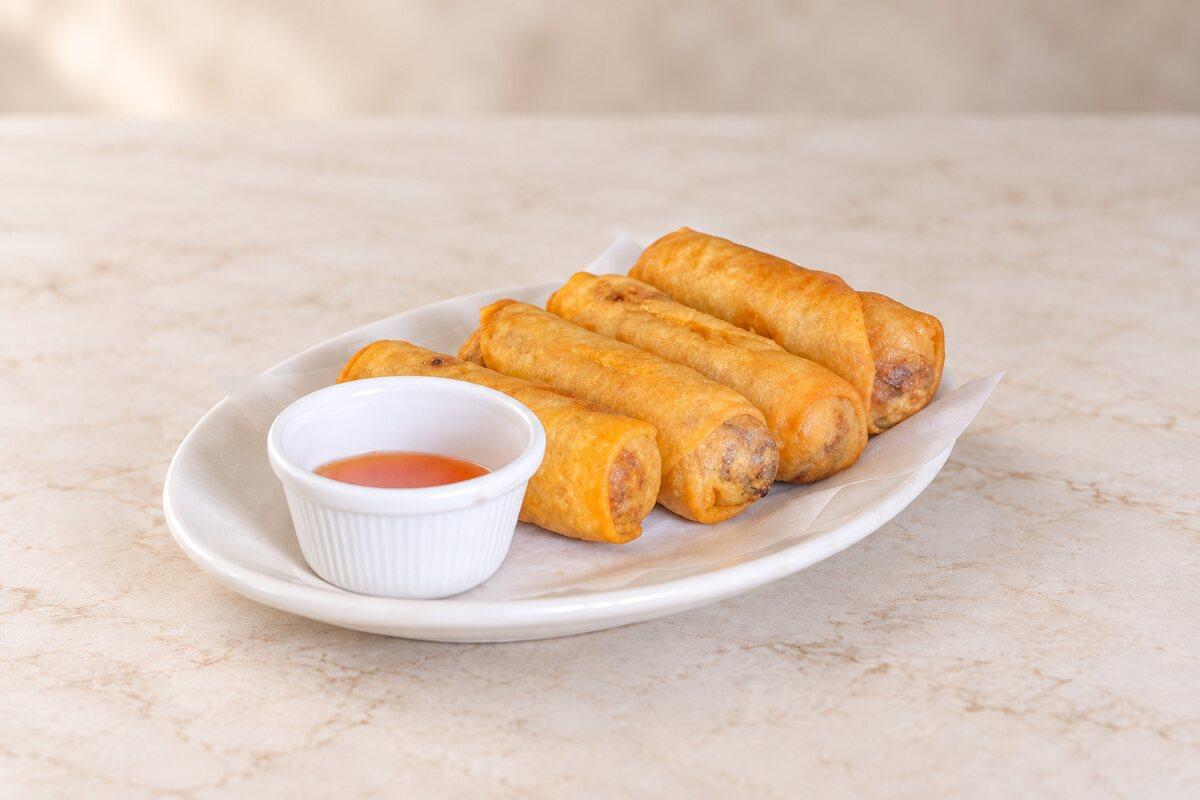 Golden fried rolls on a white plate with a small dish of sweet chilli sauce.