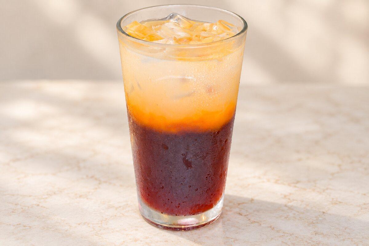 A tall glass of iced Thai tea, amber over dark.