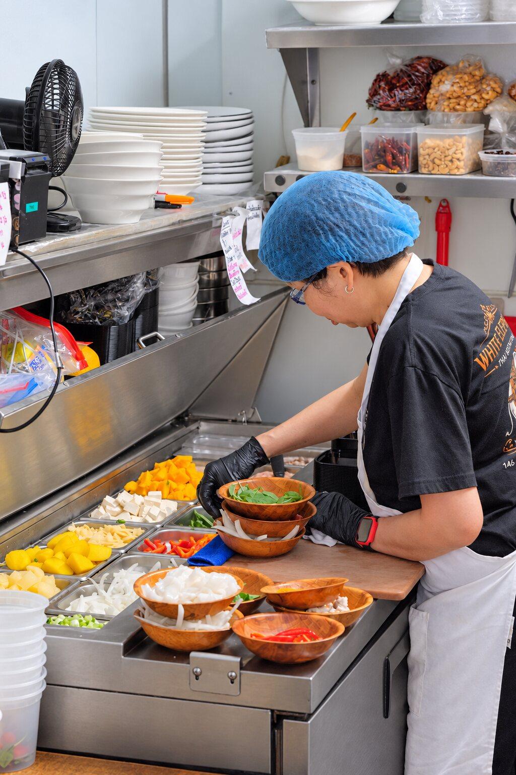 A cook at the prep counter, portioning ingredients for an order.
