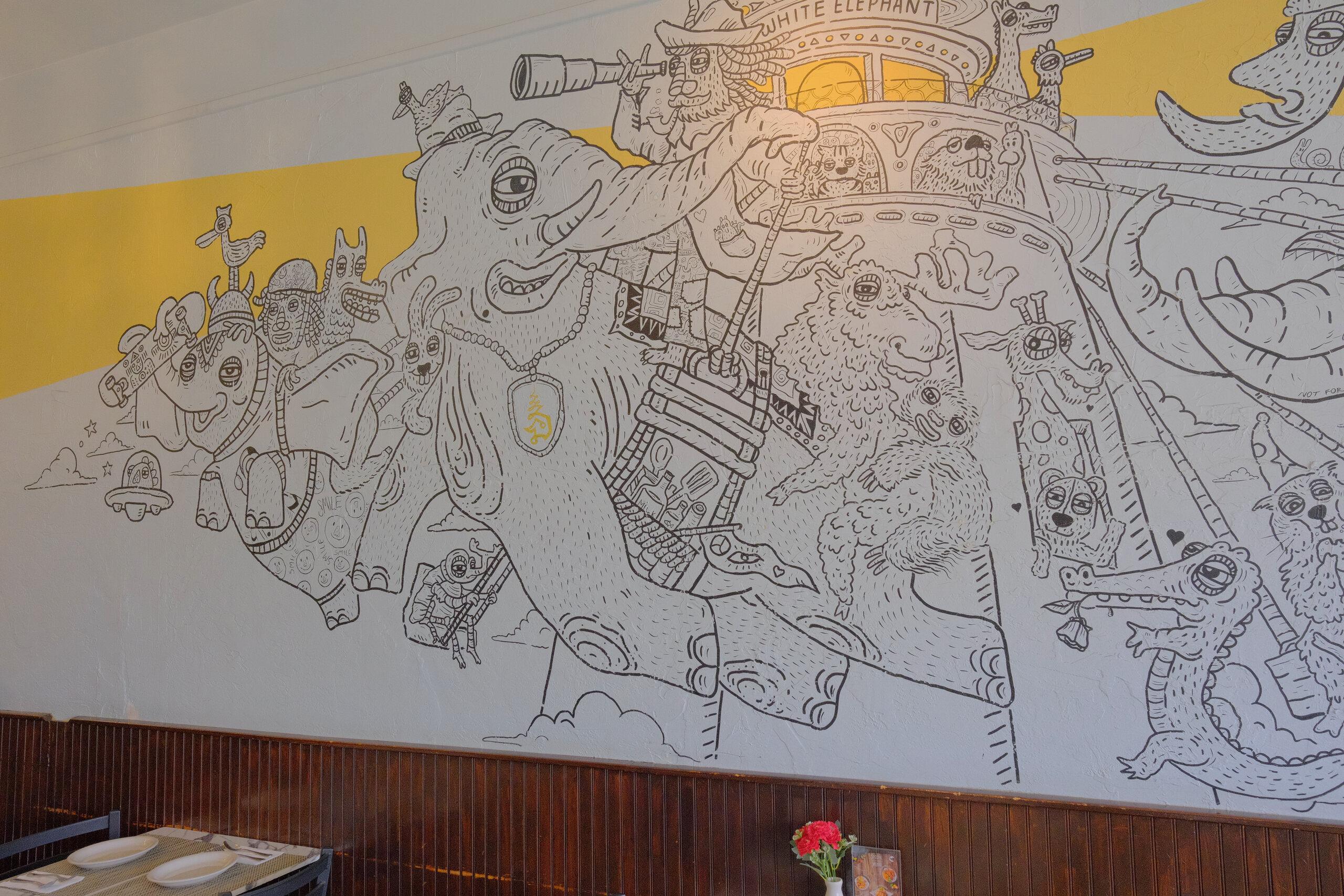 The black line-art mural along the dining room wall: an elephant carrying a crowd of characters, with a yellow band above.
