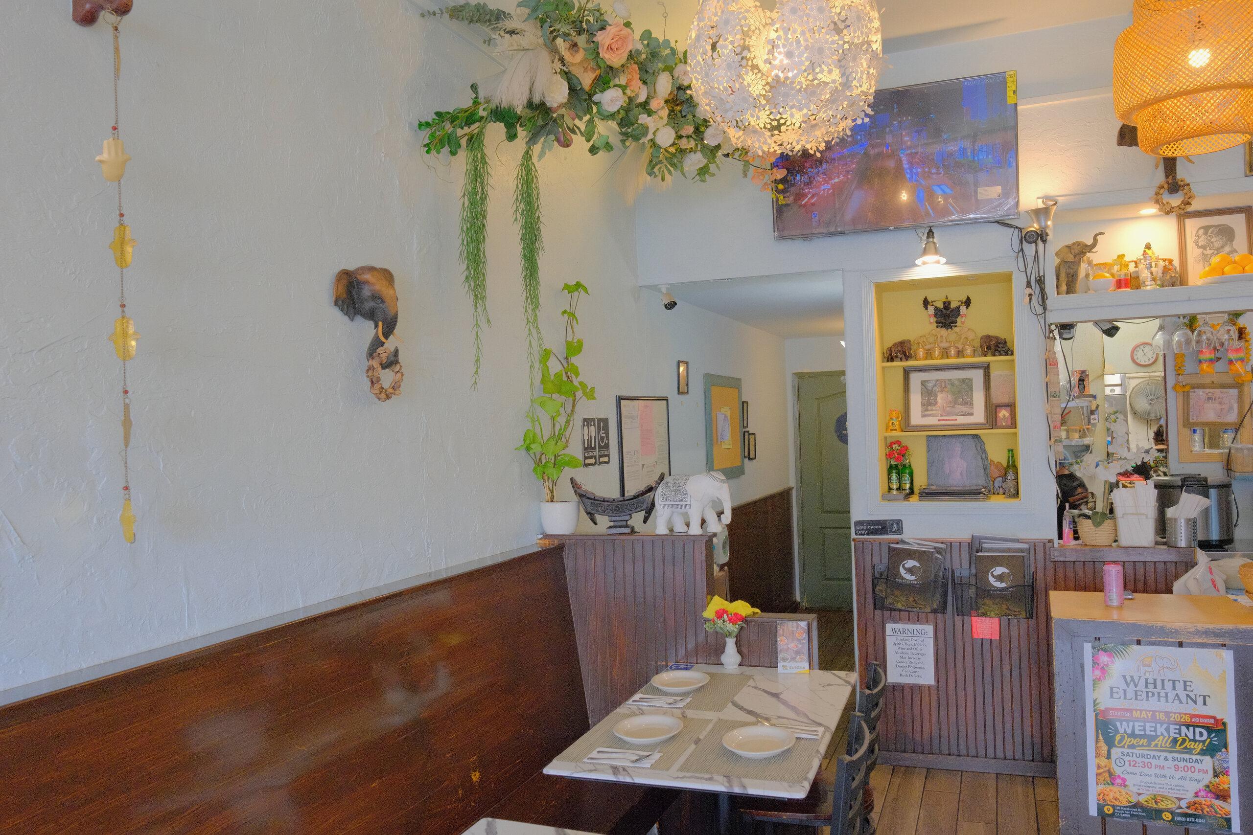 A corner of the dining room with hanging plants, a rattan lamp, a small elephant figure on the wainscot, and a set table.